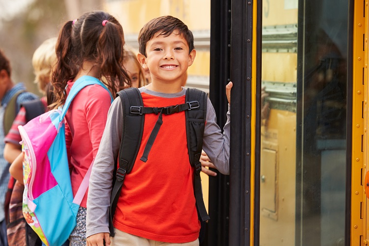 A Hispanic/Latinx boy lines up next to a school bus.