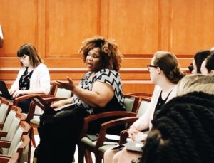 A woman sits in her set as she begins to ask a question.